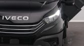 Close-up of the front end of a black Iveco truck, featuring a chrome grille and illuminated headlight.