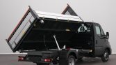Black utility truck with a large metal dump bed lifted by a hydraulic cylinder for unloading material.
