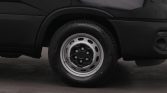 Front wheel of a black van, showing a steel rim and tire on a paved surface, partial vehicle body visible behind it