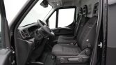 Interior of a black van showing the driver’s seat and two passenger seats, steering wheel, and dashboard with the side door open