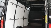 Interior of a empty cargo van with white side panels, black wheel arches, and a yellow side door handle visible at the rear