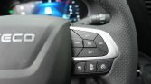 Close-up of a car steering wheel with illuminated cruise control buttons on the right, including SET+, SET−, CANCEL, RES, and the center cruise icon, plus perforated grip on the rim behind a dashboard display.