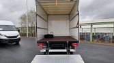 Open-back box truck with loading ramp extended, empty cargo area and a tire inside, in a parking lot.