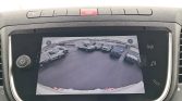 Live feed from the car's rearview camera showing a parking lot with white vans; the display is mounted in the dashboard.