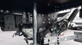 Underside of a heavy-duty trailer showing metal frame, bolts, and a vertical chrome support post with bundled cables and hoses nearby.