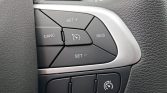 Close-up of a car steering wheel cruise-control cluster with buttons labeled SET+, CANC/CAN C, RES, and SET− around a central speedometer icon, on a black panel with a silver trim