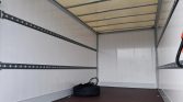 Empty box truck trailer interior with white walls, metal cargo rails along the sides, and a spare tire on the floor.