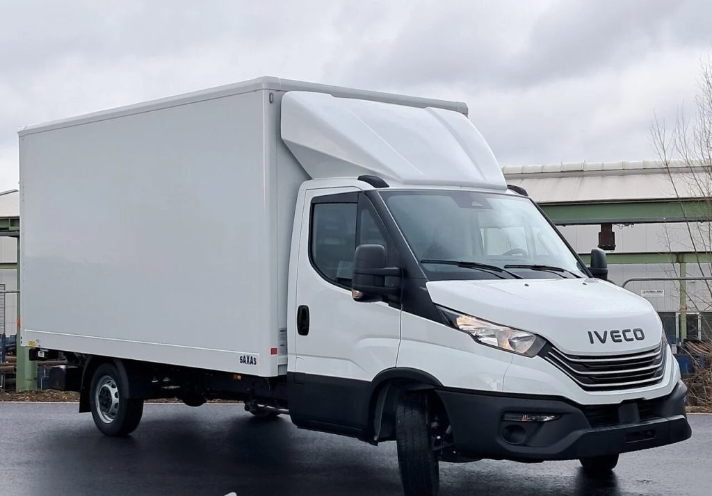 White Iveco box truck with a large cargo box, parked on a wet pavement under a cloudy sky.