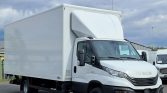 White Iveco box truck parked in a lot, showing its large cargo box from the side view on a cloudy day.