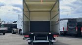 Open white box truck trailer with the rear doors up and a lowered loading ramp, empty cargo area ready to load in a parking lot.