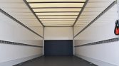 Interior of an empty cargo trailer with white walls, dark floor, and multiple side rails for securing cargo, viewed from the back doorway area.