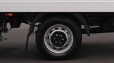 Close-up of a truck wheel with a silver rim under a white cargo trailer on a paved surface