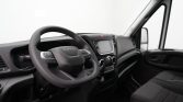 Interior of a van cockpit with steering wheel bearing the Iveco logo, center touchscreen, and gear shifter visible near the dashboard.