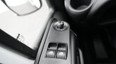 Close-up of a car's driver-side door panel with window switches and mirror adjustment knob to the left of the armrest.
