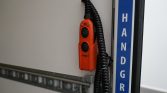 Red emergency lift control with a coiled black cord mounted on a gray panel beside a blue 'HANDGRIP' label.