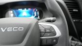 Close-up of a car steering wheel with cruise control buttons on the right and a blurred digital instrument cluster in the background.