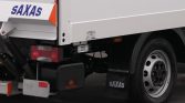 Rear view of a SAXAS delivery truck showing taillight, mudflap with SAXAS, and a black toolbox with a red logo under the chassis