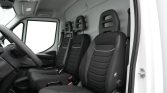 Interior of a white van showing the driver seat and two passenger seats with black fabric upholstery and visible seat belts, left-hand steering wheel present
