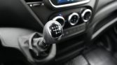 Manual gear shift knob in a car showing reverse and 1–6 gears, with the dashboard and climate controls in blurred background.