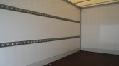 Empty truck trailer interior with white walls, two horizontal metal rails running along the side, and a brown floor.