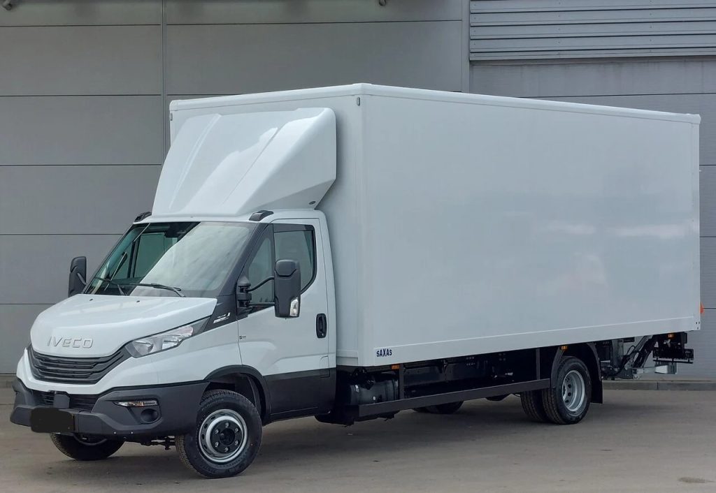 White Iveco box truck with a large cargo box parked near a gray industrial building, showing the cab and front end clearly.