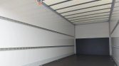 Interior of an empty white cargo trailer with metal side rails and a dark rear bulkhead at the far end.