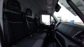 Interior of a cargo van: three black fabric seats with belts, front dashboard and steering wheel visible, large windows showing trucks outside