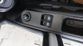 Car door panel with two window switches and a circular side mirror adjustment knob to the left.