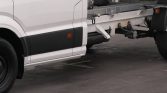 Partial side view of a white commercial truck cab with exposed chassis and rear wheel visible on the left in an indoor setting