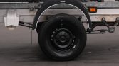 Close-up of a trailer wheel with a black steel rim and white curved fender, mounted on a flatbed trailer edge.