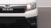 Front view of a white MAN truck, showing the logo, grille, and a lit headlight on the right side of the image.