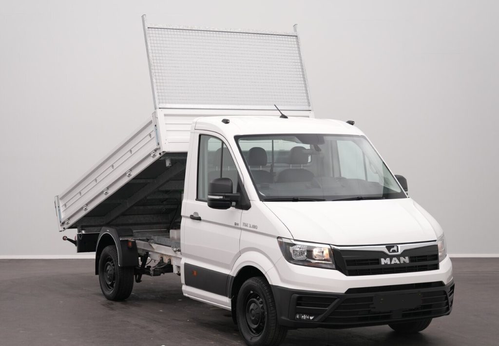 White MAN dump truck with tilted steel bed in a studio setting, ready to unload gravel or debris, side facing camera
