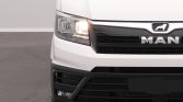 Front view of a white MAN truck with the headlight on, showing the grille and logo.