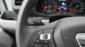 Close-up of a car steering wheel showing cruise control buttons on the left and a blurred instrument cluster in the background.