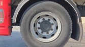 Close-up of a heavy truck wheel: gray steel rim with lug nuts and a chunky tire, red fuel tank visible on the left and a black fender above