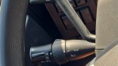 Close-up of a car steering column with the headlight/fog light control stalk and turn signal icons near the wheel, showing the left-side controls.