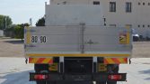 Rear view of a gray flatbed truck with '80 90' markings, yellow safety stripes, and a blind-spot warning sticker on the right side.