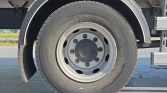 Close-up image of a truck wheel and tire with a steel rim and lug nuts, mudguard nearby, on a paved surface
