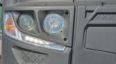 Close-up of a gray truck's front left headlight area showing round main headlight, a smaller circular fog/auxiliary light, an amber turn signal, and a lower LED strip along the bumper.