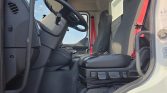 Interior of a truck cab showing the driver's seat, steering wheel, and passenger seat with red seatbelts.