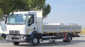 White Renault flatbed truck parked on a sunny lot with trees in the background, ready for loading