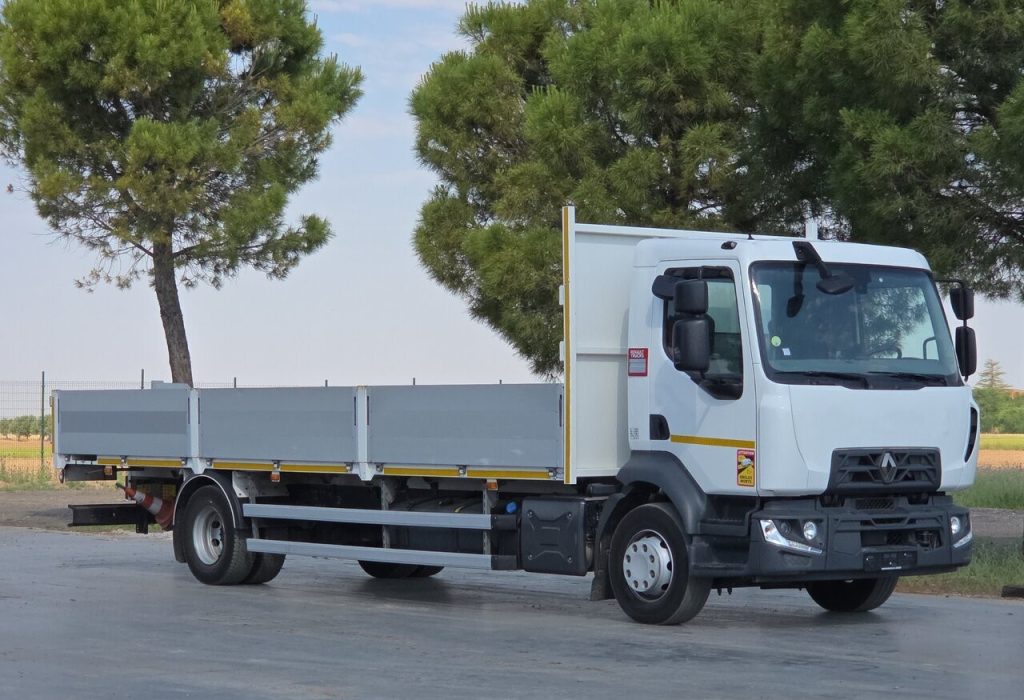 White cab-over flatbed truck with gray side rails parked on a paved lot, trees in the background, ready for loading or transport.