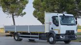 White cab-over flatbed truck with gray side rails parked on a paved lot, trees in the background, ready for loading or transport.