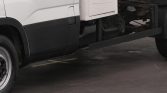 Side view of a white commercial truck with black lower trim; a metal rail runs along the chassis near the rear undercarriage.