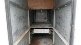 Interior of a dirty, narrow metal shaft or cabinet with gray walls and a small metal platform mid-way, viewed from the opening.