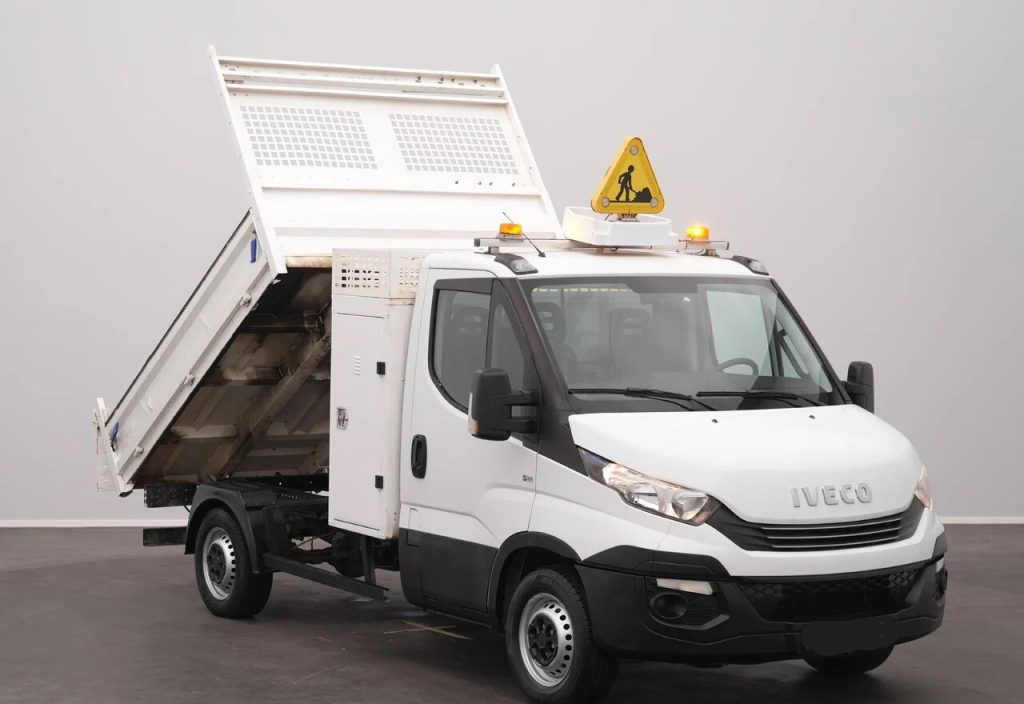 White Iveco utility truck with a raised dumping bed indoors, and a yellow warning sign on the roof.