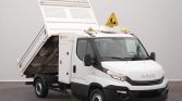 White Iveco utility truck with a raised dumping bed indoors, and a yellow warning sign on the roof.