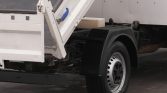 Rear of a white dump truck with its tailgate lowered and ramp resting on the bed edge.