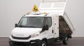 White Iveco utility dump truck with its cargo bed raised, amber beacon lights on and a yellow warning sign on top.