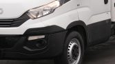 Front-left view of a white cargo van, showing the headlight, grille, and front wheel on a dark pavement surface.